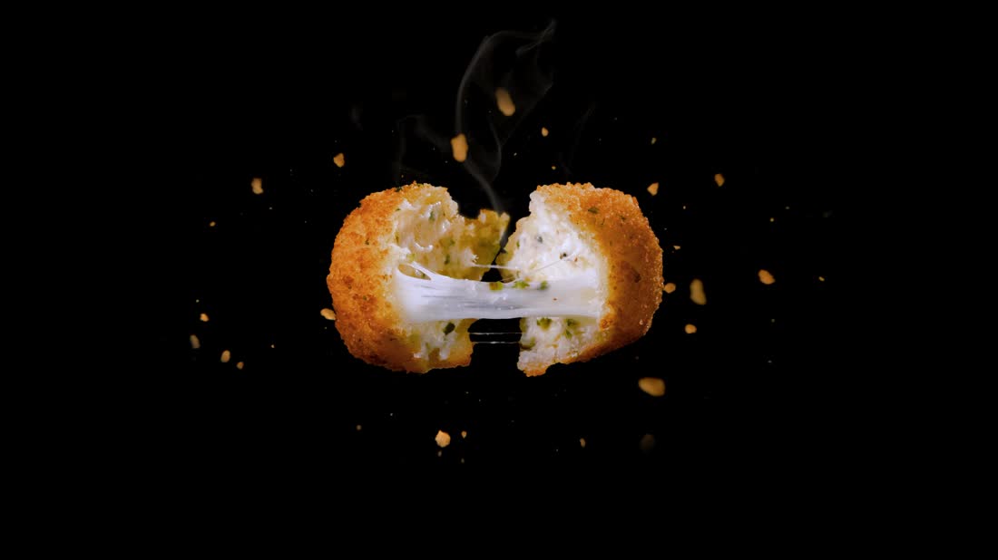 Close-up of a fried ricotta bite with melted cheese pulling apart, surrounded by crumbs