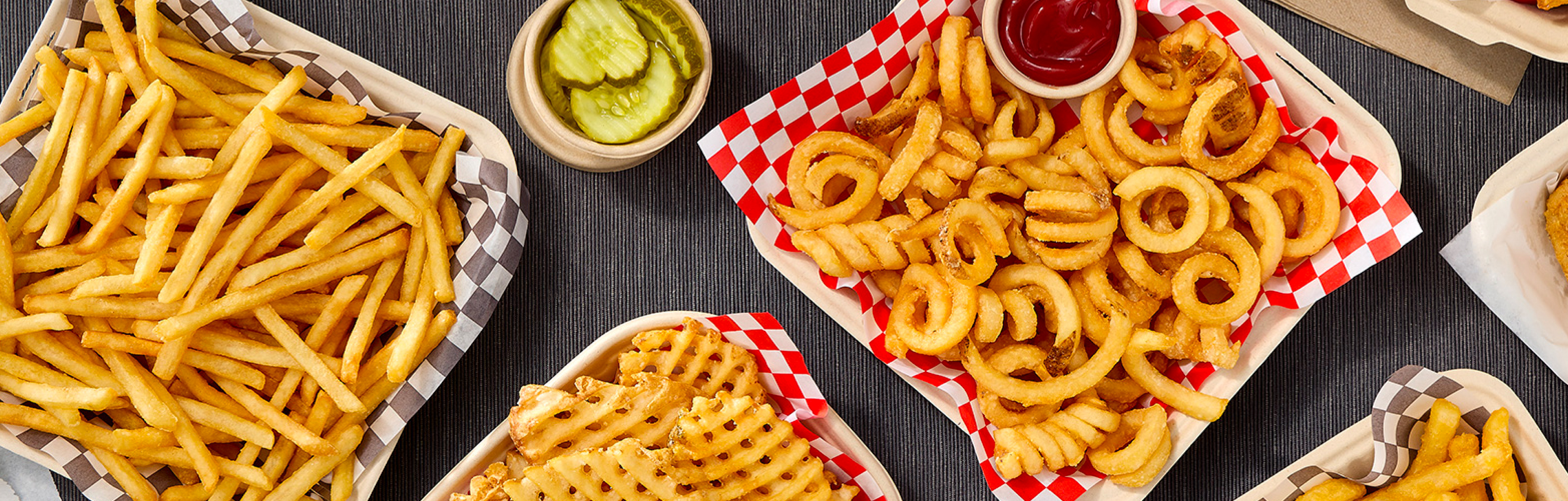 Various McCain® fries, including straight- cut, curly and waffle fries in a basket with a side of ketchup
