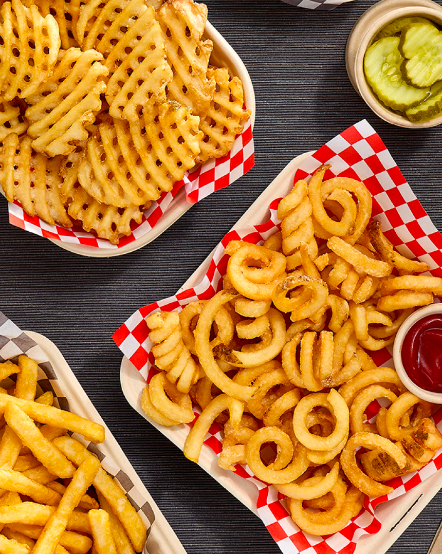 Various McCain® fries, including straight- cut, curly and waffle fries in a basket with a side of ketchup