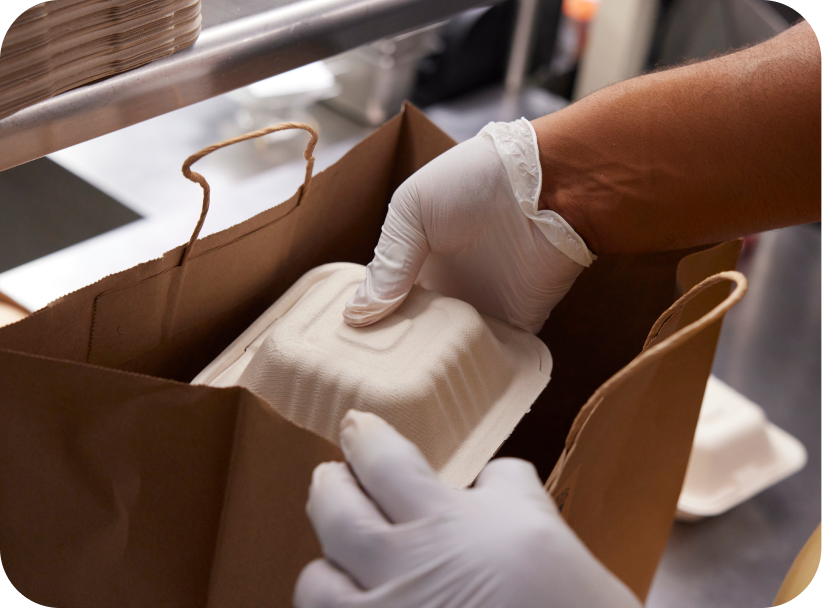 Foodservice staff member placing a to-go box of McCain® SureCrisp® fries into a bag for a delivery order.