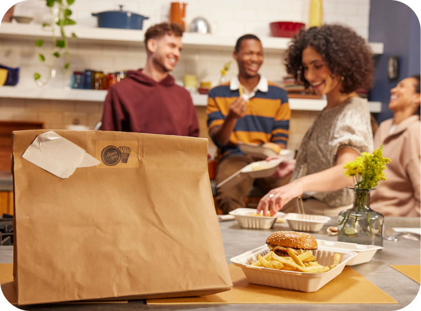 Friends enjoying a delivery order of McCain® SureCrisp® fries and burgers in a kitchen setting.