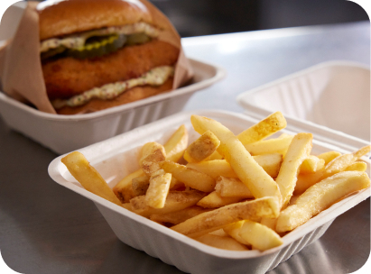 Close-up of McCain® SureCrisp® fries and a crispy chicken sandwich in takeout boxes.