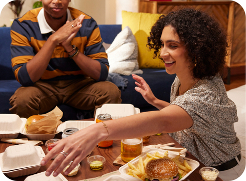 Group of friends enjoying takeout orders of McCain® SureCrisp® fries and burgers together.